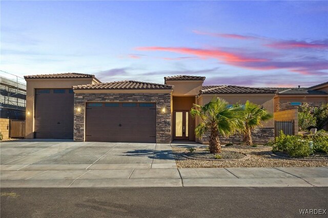 mediterranean / spanish-style home with driveway, a garage, stone siding, a tile roof, and stucco siding