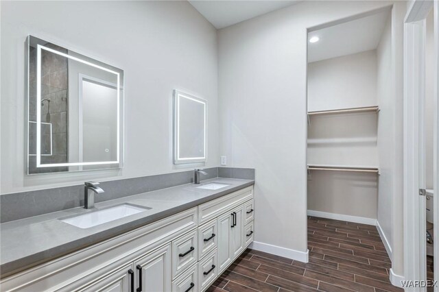 full bathroom featuring a walk in closet, double vanity, a sink, and wood tiled floor