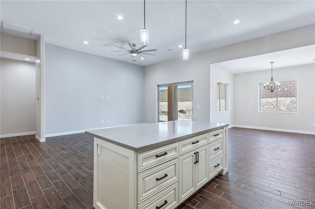 kitchen with ceiling fan with notable chandelier, open floor plan, a center island, wood tiled floor, and pendant lighting