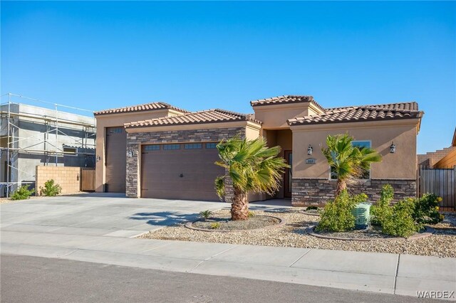 mediterranean / spanish-style house with a garage, driveway, stone siding, a tile roof, and stucco siding