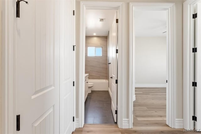 hallway featuring light wood-style flooring, visible vents, and baseboards