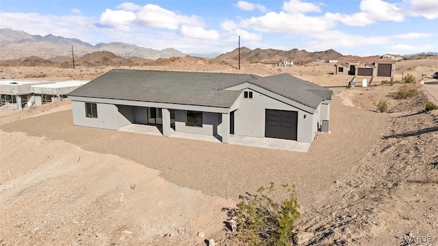 view of front of property with dirt driveway, stucco siding, a mountain view, and a garage