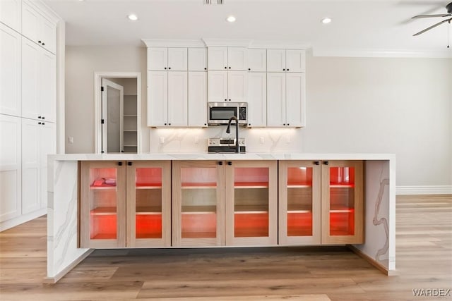 kitchen featuring appliances with stainless steel finishes, light wood-type flooring, white cabinets, and tasteful backsplash