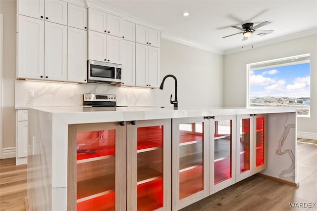 kitchen with tasteful backsplash, light countertops, appliances with stainless steel finishes, light wood-style floors, and ornamental molding