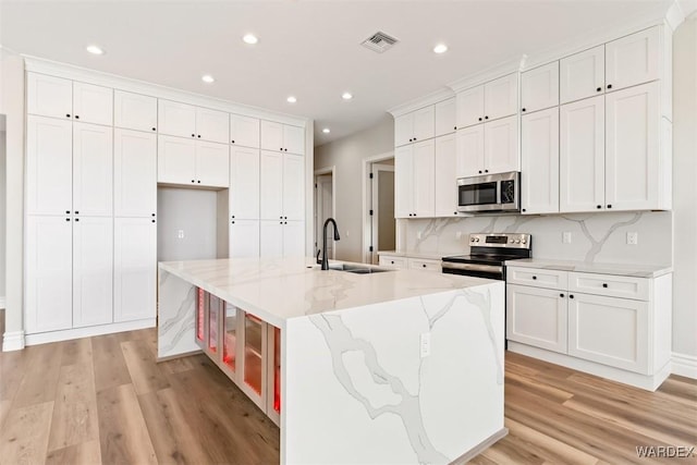 kitchen featuring light wood-style flooring, stainless steel appliances, a sink, visible vents, and a large island with sink