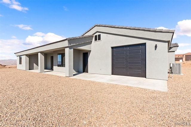 view of front of house with an attached garage, a patio area, and stucco siding