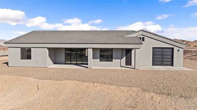 rear view of property with an attached garage and stucco siding