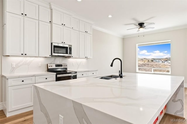 kitchen with light wood finished floors, a large island, appliances with stainless steel finishes, ornamental molding, and a sink