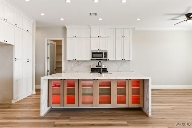 kitchen with visible vents, white cabinets, appliances with stainless steel finishes, light wood-style floors, and backsplash