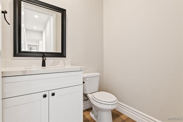 bathroom featuring toilet, baseboards, wood finished floors, and vanity