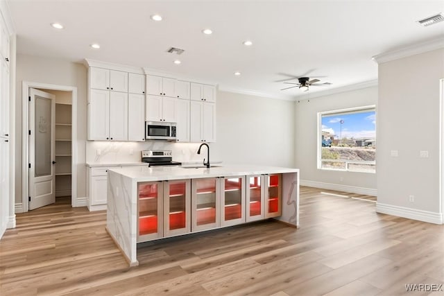 kitchen with visible vents, appliances with stainless steel finishes, ornamental molding, a kitchen island with sink, and light countertops