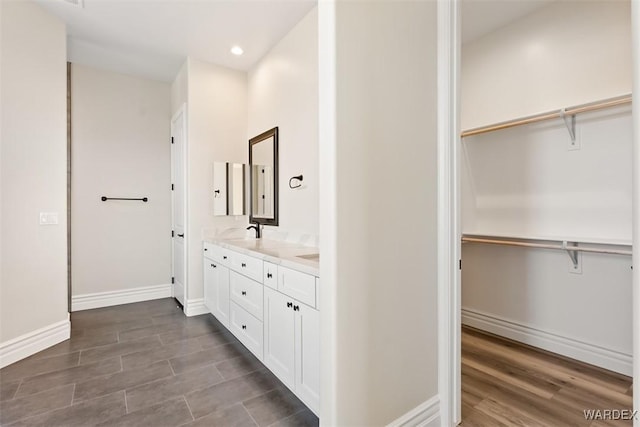 bathroom featuring double vanity, baseboards, wood finished floors, a spacious closet, and a sink