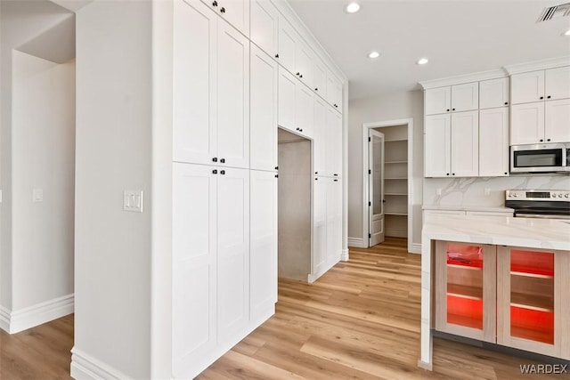 kitchen featuring visible vents, backsplash, appliances with stainless steel finishes, light wood-style floors, and light stone countertops