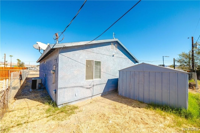 view of property exterior with an outbuilding, a storage unit, fence, central air condition unit, and stucco siding