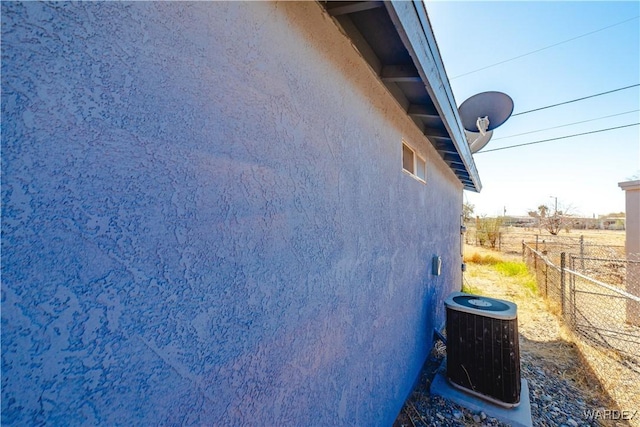 view of side of home featuring central air condition unit, fence, and stucco siding