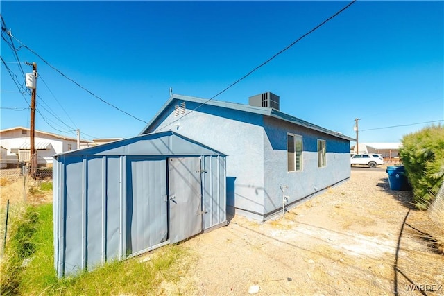 back of house featuring cooling unit, an outdoor structure, fence, stucco siding, and a shed