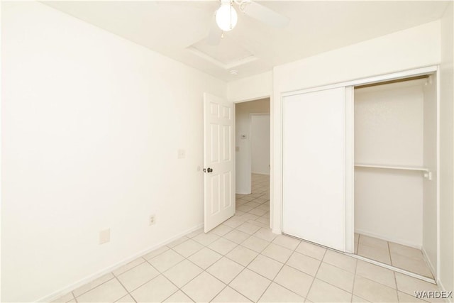 unfurnished bedroom with light tile patterned floors, a closet, attic access, ceiling fan, and baseboards