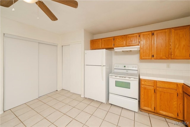 kitchen with white appliances, light tile patterned floors, brown cabinetry, light countertops, and under cabinet range hood