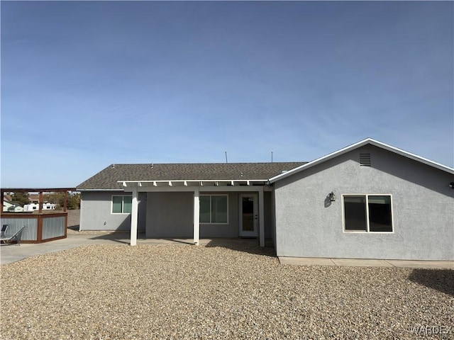 rear view of house with roof with shingles, a patio area, and stucco siding