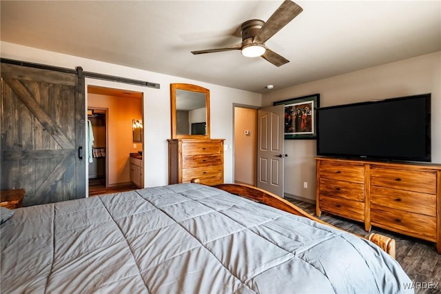 unfurnished bedroom with a barn door, a ceiling fan, wood finished floors, and ensuite bathroom