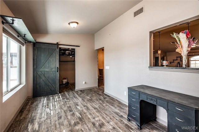 unfurnished office featuring a barn door, wood finished floors, visible vents, and baseboards