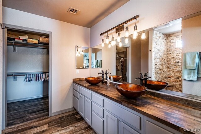 full bath featuring a walk in closet, a sink, and wood finished floors