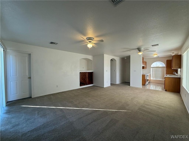 unfurnished living room with ceiling fan, visible vents, arched walkways, and carpet flooring