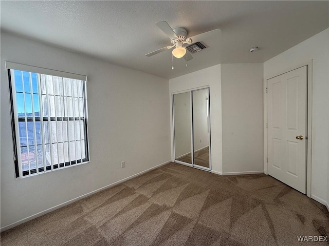 unfurnished bedroom featuring carpet floors, a closet, visible vents, a ceiling fan, and baseboards