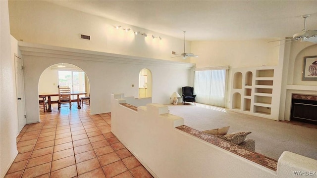 interior space featuring ceiling fan, built in features, arched walkways, and a fireplace with flush hearth