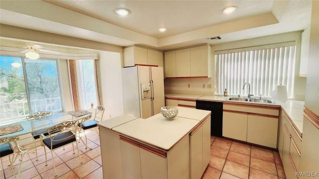 kitchen featuring white refrigerator with ice dispenser, a raised ceiling, light countertops, a kitchen island, and a sink