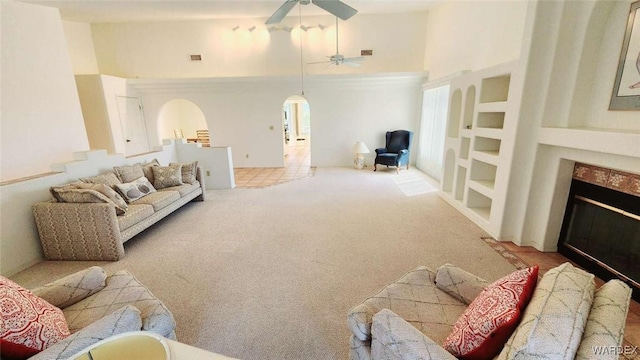 carpeted living room featuring arched walkways, visible vents, a high ceiling, a ceiling fan, and a glass covered fireplace