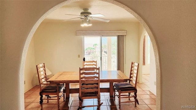 dining area with arched walkways, ceiling fan, and light tile patterned floors