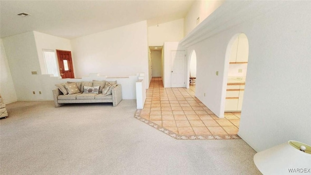 unfurnished living room with arched walkways, light tile patterned floors, visible vents, a towering ceiling, and light carpet