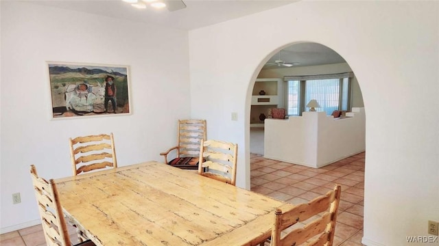 dining area featuring arched walkways, ceiling fan, and light tile patterned floors