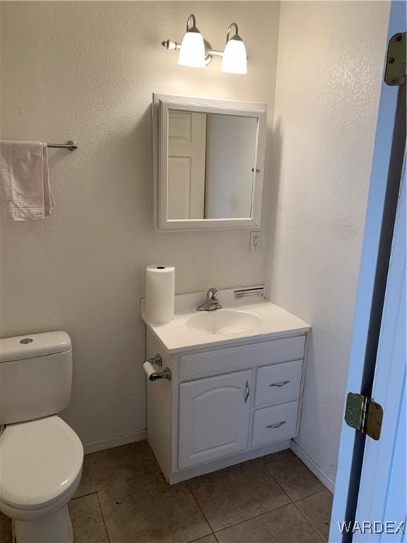 half bath featuring baseboards, vanity, toilet, and tile patterned floors