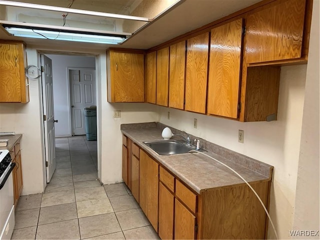 kitchen featuring light tile patterned floors, stove, a sink, and brown cabinetry