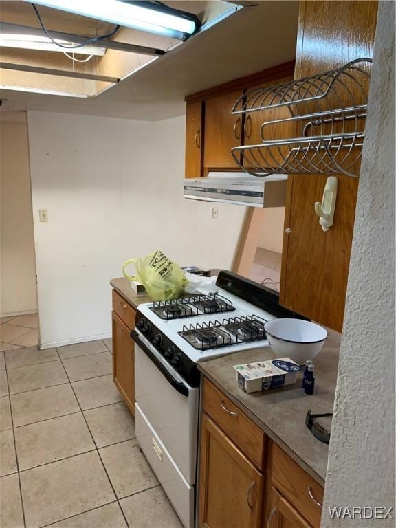 kitchen featuring dark countertops, brown cabinets, white gas stove, and light tile patterned floors