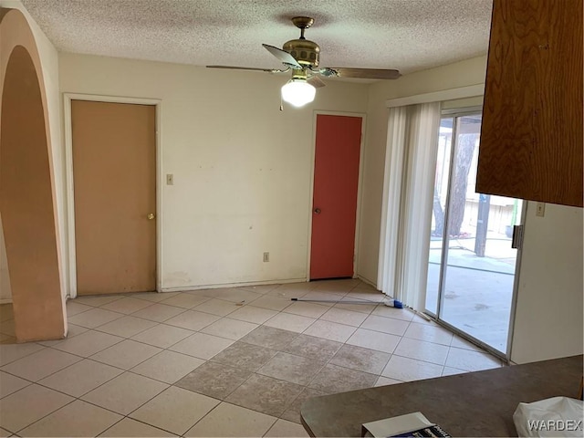 spare room with ceiling fan, a textured ceiling, light tile patterned flooring, and arched walkways