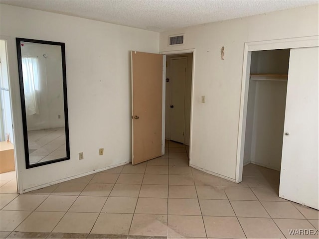 unfurnished bedroom with light tile patterned floors, a textured ceiling, a closet, and visible vents