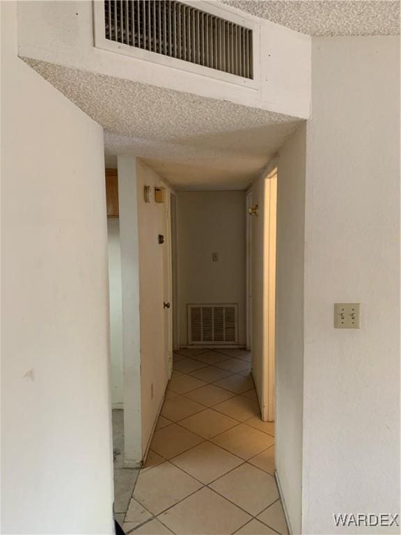 corridor featuring visible vents, a textured ceiling, and light tile patterned flooring