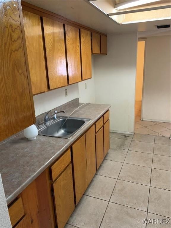 kitchen featuring light tile patterned flooring, a sink, visible vents, and brown cabinets