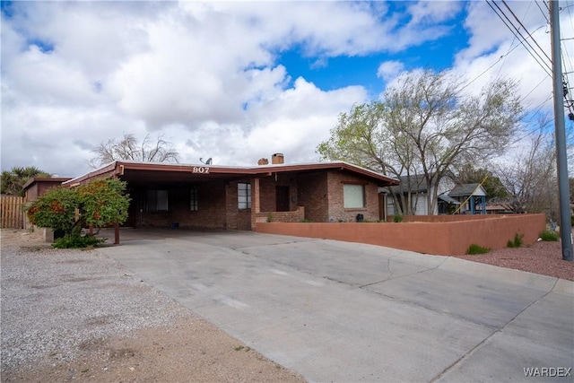 ranch-style house with an attached carport, fence, driveway, a chimney, and brick siding