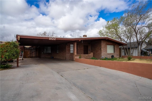 view of front facade featuring a carport, driveway, a chimney, and brick siding