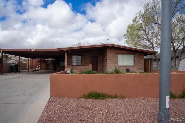 view of front facade with a carport, concrete driveway, brick siding, and fence