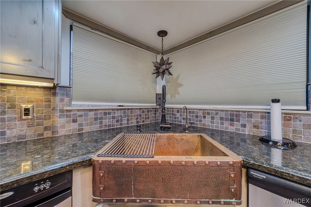 kitchen with dishwasher, dark stone countertops, a sink, and decorative backsplash