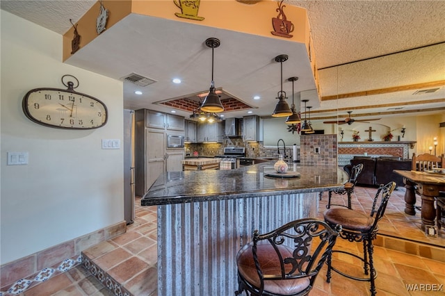 kitchen with tasteful backsplash, dark countertops, visible vents, a peninsula, and wall chimney exhaust hood