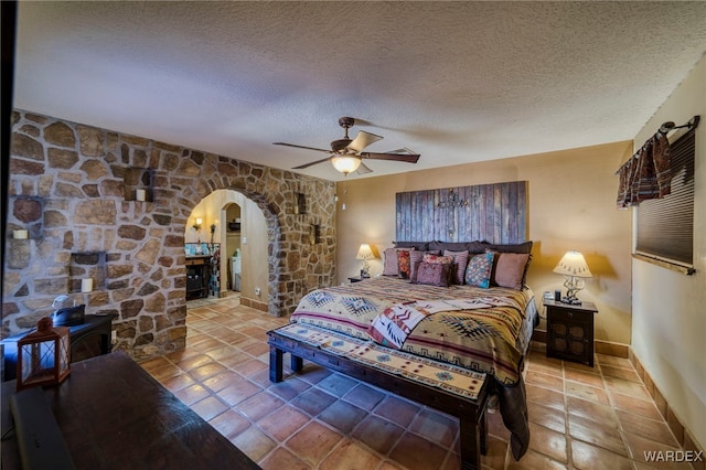 bedroom featuring arched walkways, tile patterned flooring, a textured ceiling, and baseboards