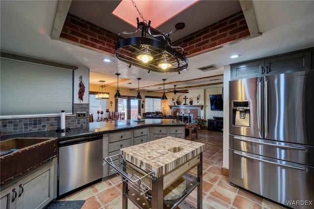 kitchen featuring stainless steel appliances, a fireplace, visible vents, backsplash, and stone tile flooring