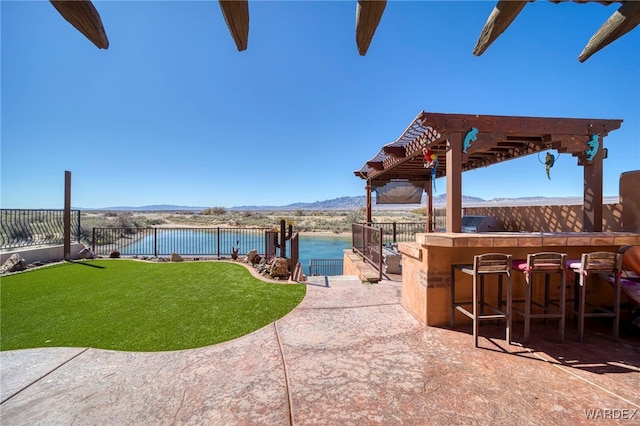 view of patio / terrace featuring an outdoor kitchen, fence, outdoor dry bar, a water and mountain view, and a pergola