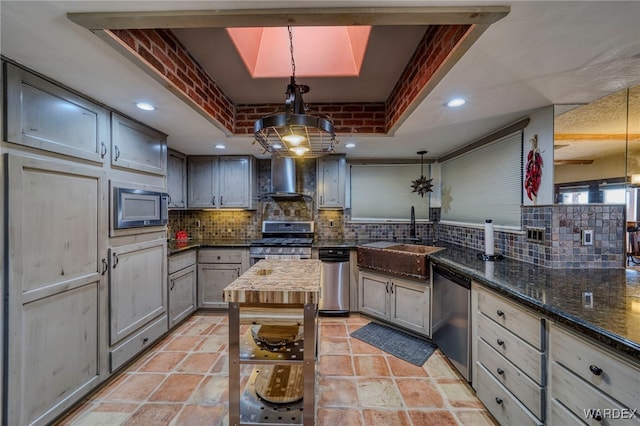 kitchen with a tray ceiling, tasteful backsplash, appliances with stainless steel finishes, a sink, and wall chimney range hood